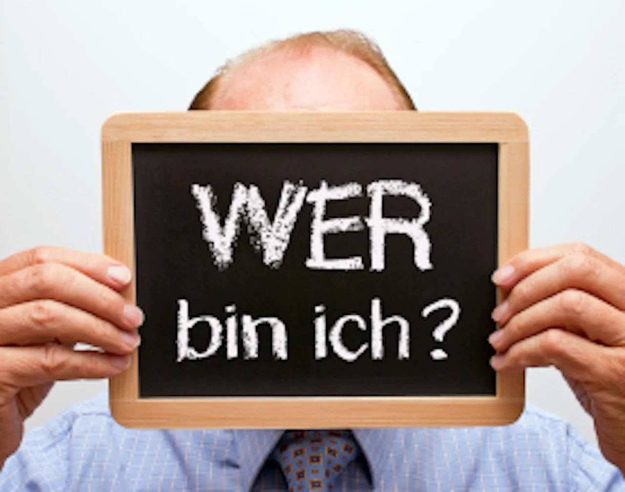 FokusDEMENZ - ein Mann hält eine Kreidetafel, auf der der Text „WER bin ich“ steht 